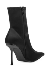 Bota negra hasta el tobillo con tacón de stilettos alto, fabricada en tejido elástico, diseño de punta afilada, cierre lateral con cremallera y detalles de costura.