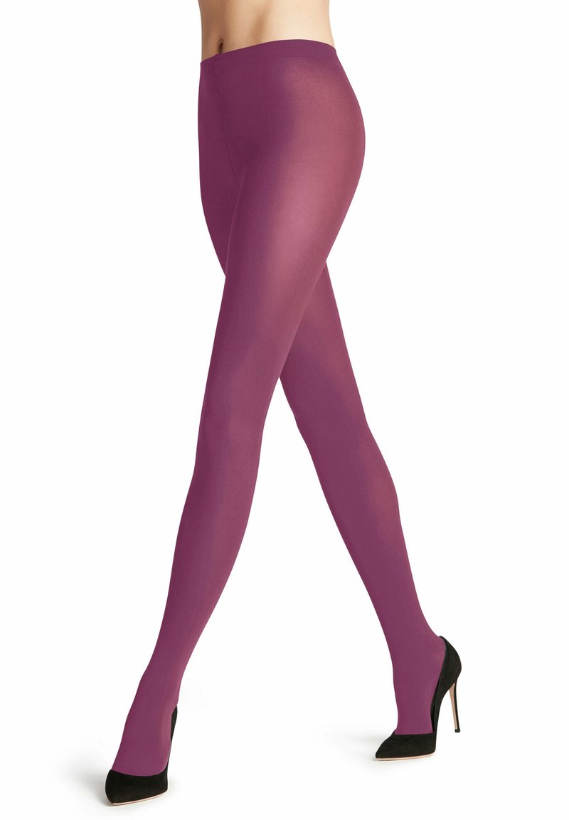 Donna che indossa collant trasparenti viola e scarpe nere con tacco alto, in piedi con le gambe incrociate su uno sfondo bianco.