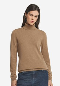 Brązowy sweter typu golf z długimi rękawami, ściągaczami na mankietach i luźnym fasonem. Miękka faktura i minimalne elementy designu.
