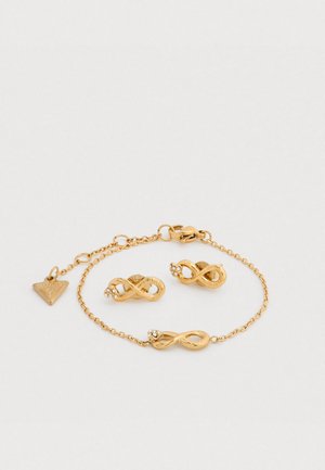 Ensemble de bijoux dorés comprenant deux clous d'oreille en forme d'infini et un bracelet assorti avec de petits accents de strass et une chaîne réglable.