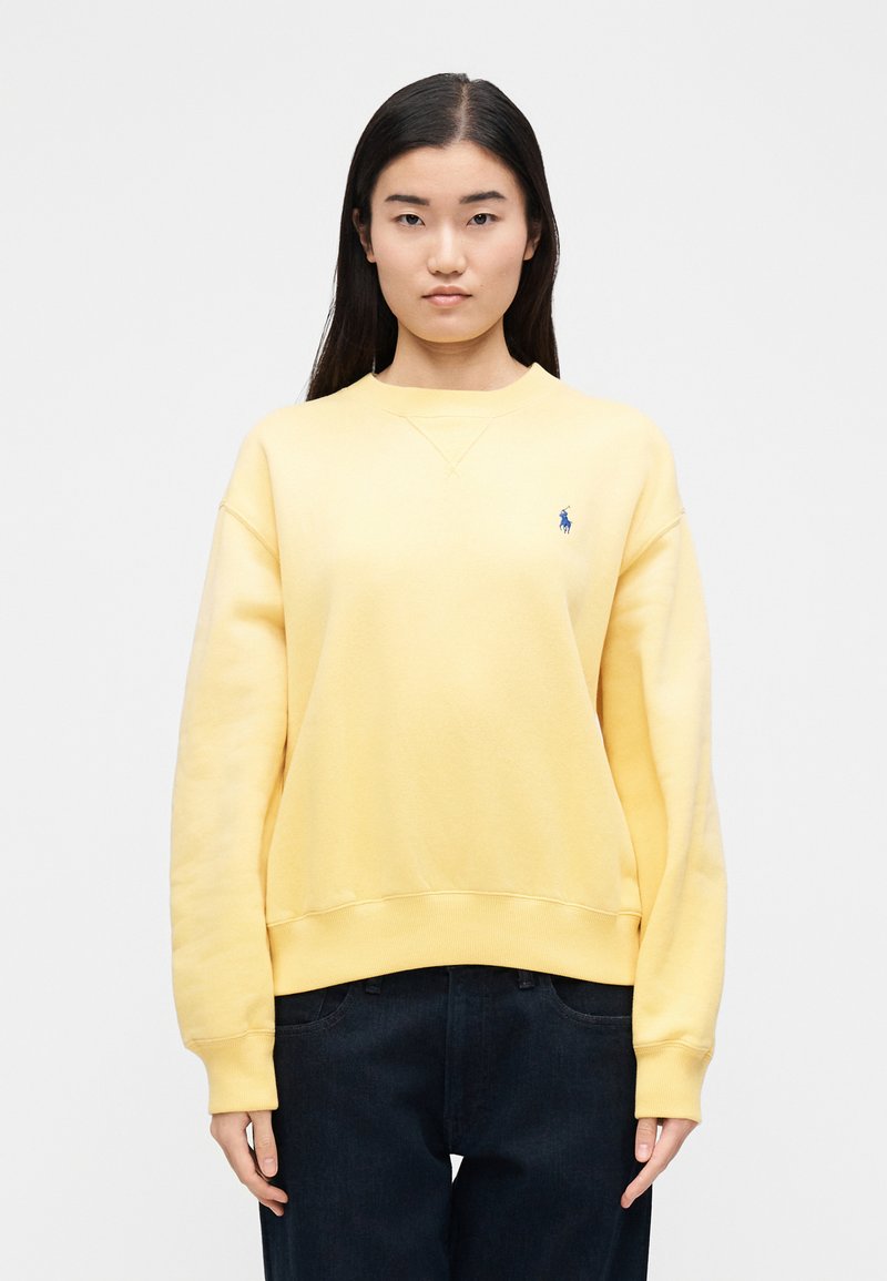 Sweat-shirt jaune en mélange de coton doux avec un col rond, des poignets côtelés et un petit logo brodé bleu sur la poitrine.