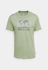 Camiseta de algodón verde claro con un gráfico de un globo y el texto "NIKE" en negro, cuello redondo, mangas cortas y dobladillo recto.