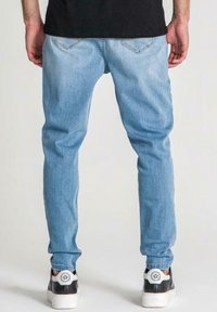 Ljust blå denimjeans med slim fit, med bakfickor och en urtvättad textur. Matchas med svarta och vita sneakers.