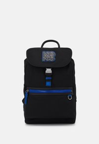 Sac à dos noir en tissu résistant avec un rabat pliable, une fermeture éclair bleue et un patch logo bleu et blanc. Il dispose d'une poignée supérieure et d'une poche avant.