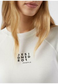 Jasnoszara bluza z dzianiną prążkowaną przy dekolcie i raglanowymi rękawami, z czarnym nadrukiem tekstu w pogrubionej czcionce, brzmiącym "DESIGNED FOR PEOPLE."