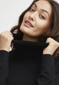 Maglione nero a collo alto con texture a coste, dotato di un colletto alto e maniche lunghe. Il tessuto appare morbido ed elastico.