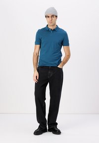 Herre teal polo skjorte, svarte denim bukser, grå strikket lue og svarte sko. Polo skjorten har krage og tre knapper.