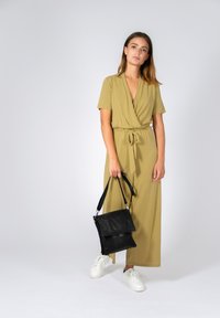 Abito avvolgente verde oliva, con maniche corte e vita con lacci, abbinato a sneakers bianche e una borsa a tracolla in pelle nera. Tessuto liscio, vestibilità comoda.