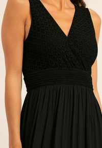 Robe noire avec un corsage texturé tissé, un décolleté en V, une taille smockée et une jupe fluide et froncée. Le tissu lisse offre une finition douce.