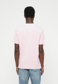 Tricou roz deschis din bumbac, cu mâneci scurte și guler rotund, având o textură moale și tiv drept, purtat cu blugi albaștri.