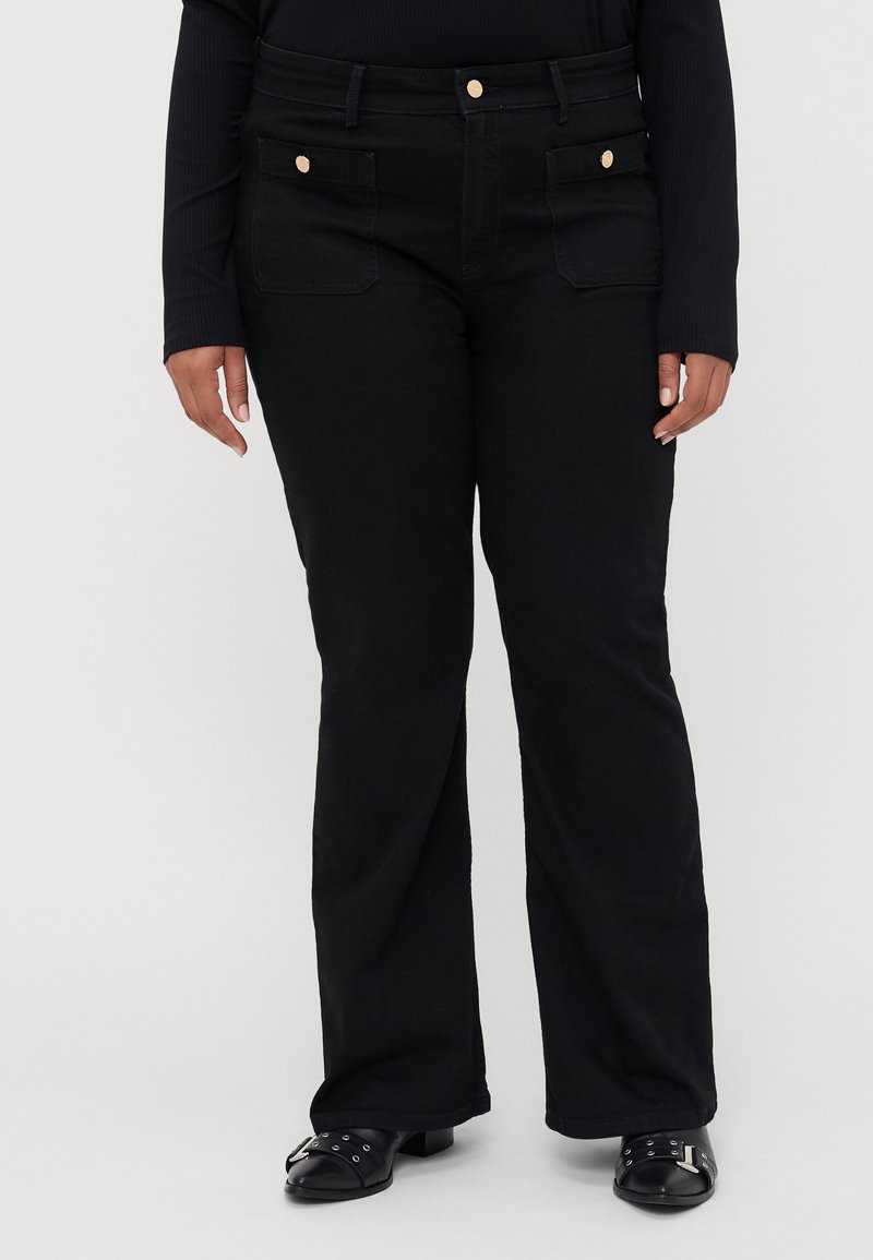 Black flared pants in a cotton blend with front pockets and gold-tone buttons. Smooth texture with a relaxed fit, paired with black shoes.