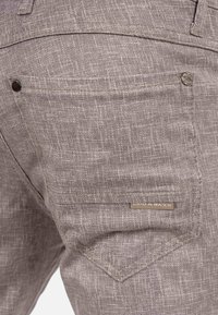 Grijze stoffen broek met een gestructureerd patroon, contrasterende stiksels, een achterzak met een decoratief label en een gladde afwerking.