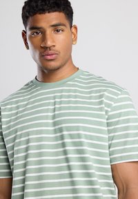 T-shirt verde a righe con strisce orizzontali bianche, maniche corte, scollatura a girocollo e una texture morbida e liscia.