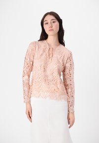 Spitzenbluse in hellem Pfirsich mit Blumenmuster, langen Ärmeln, V-Ausschnitt mit Bindeband und gewelltem Saum. Aus feiner Spitzenmaterial gefertigt.