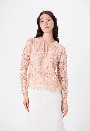 Blonde bluse i lys fersken med blomstermønster, lange ermer, v-hals med knytedetalj og bølget kant. Laget av intrikat blondermateriale.