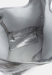 Silver äkta läder tote-väska med en slät, glänsande insida och en dragkedjeficka. Insidan har mjuk textur och minimalistisk design.
