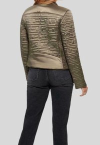 Veste matelassée vert olive au design élégant, présentant un dos texturé et un devant lisse. Portée avec un jean foncé, vue de dos.