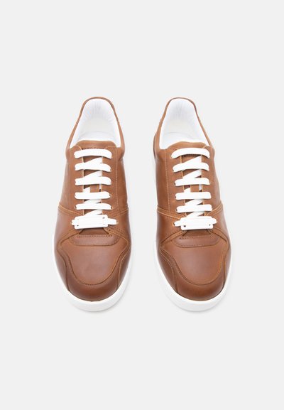 Ζευγάρι καφέ δερμάτινα αθλητικά παπούτσια με λευκά κορδόνια και λευκές σόλες, εμφανισμένα από πάνω σε ανοιχτό γκρι φόντο.