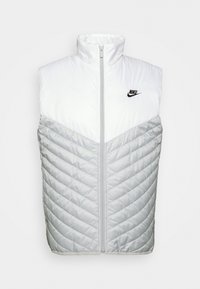 Vadderad ärmlös väst i vitt och ljusgrått. Diamantquiltad textur på den nedre halvan. Har hög krage och framdragkedja, med en svart logotyp.