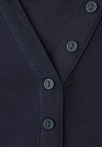 Close-up van donkerblauwe gebreide veststof met drie bijpassende ronde knopen op het voorpand.