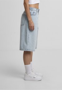 Lyseblå denimshorts med afslappet pasform, der har lommer og syninger som detaljer, sidder lige over knæet, kombineret med hvide sneakers og strømper.