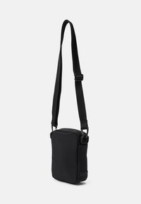 Borsa a tracolla nera realizzata in tessuto testurizzato con tracolla regolabile, forma rettangolare e design minimalista senza hardware visibile.