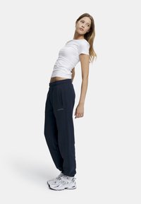 Hvit tettsittende t-skjorte kombinert med mørkeblå joggebukser med sidelommer og logo, suppleret med hvite joggesko.