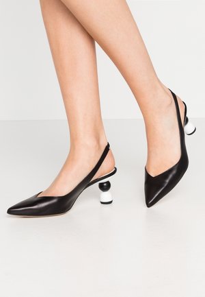 Escarpins slingback noirs pointus avec des talons ronds empilés noirs et blancs uniques, portés sur des jambes croisées sur un fond uni.