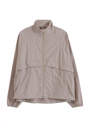 Vaaleanbeige vetoketjullinen tuulitakki, jossa on korkea kaulus, joustavat hihansuut ja vinot sivutaskut, suunniteltu rentoon käyttöön.