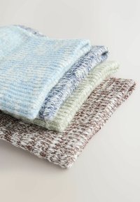 Pile de quatre articles en tissu tricoté pliés en bleu, gris, vert et marron, mettant en valeur des motifs tissés texturés sur une surface claire.