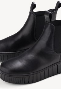 Bottines Chelsea en cuir noir avec panneaux élastiques sur les côtés, bout rond et épaisse semelle texturée présentant des rainures verticales pour une meilleure adhérence.