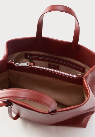 Grand sac fourre-tout en cuir rouge ouvert avec intérieur beige, double poignée et une poche intérieure zippée avec un onglet de tirage en cuir.