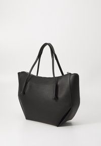 Sac cabas en cuir noir à texture lisse, forme angulaire, deux longues poignées et fermeture zippée sur le dessus. Conçu avec des accents minimalistes.