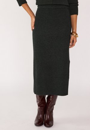Gonna maxi in maglia verde scuro con dettaglio a coste sull'orlo, abbinata a stivali al ginocchio in pelle marrone, caratterizzati da una texture liscia e una silhouette aderente.