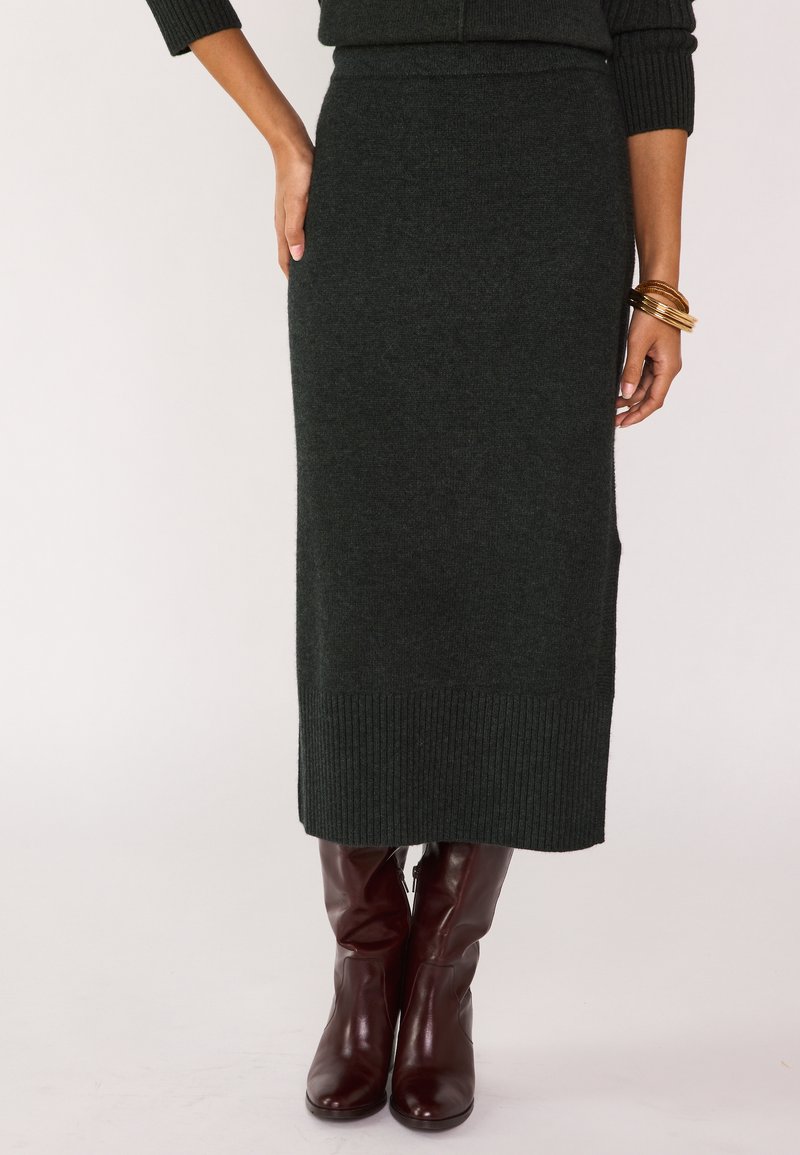 Gonna maxi in maglia verde scuro con dettaglio a coste sull'orlo, abbinata a stivali al ginocchio in pelle marrone, caratterizzati da una texture liscia e una silhouette aderente.