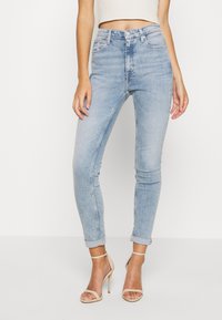 Högmidjade ljusblå jeans med slim fit, blekt utseende, femficksdesign och upprullade fållar. Modellen bär beige klackar med remmar.