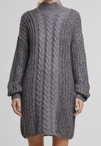 Robe pull en maille grise surdimensionnée avec des motifs en câble et en côtes, des manches ballon longues et un col haut en côtes.