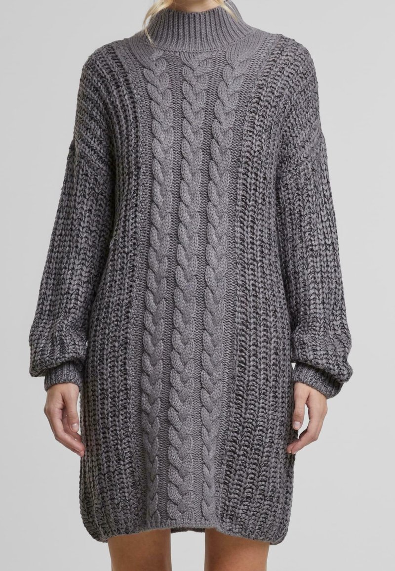 Robe pull en maille grise surdimensionnée avec des motifs en câble et en côtes, des manches ballon longues et un col haut en côtes.