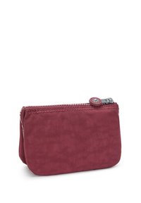 Portafoglio di tessuto rosso con chiusura a zip, forma arrotondata e un accentuato bottone decorativo sulla parte superiore. La texture appare liscia e leggermente lucida.