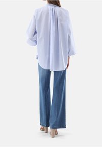 Light blue and white striped shirt with a round collar and back pleat, paired with high-waisted, wide-leg denim jeans and beige heels.