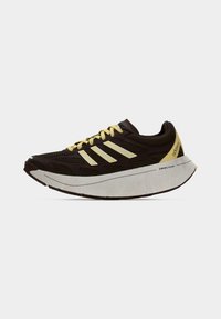 Tumepruun Adidas jooksujalanõu kollaste paelte, kollase kannatabade, valge paksu tallaga, millel on silt "SWIRLFOAM", ja hästi ventileeritud üleosaga.