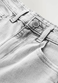 Grå denimjeans med en metallknapp och bälteshällor. Närbilden betonar tygtexturen och sömnadsdetaljerna.