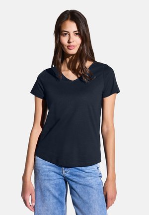 Marineblauwe T-shirt met korte mouwen van zachte stof, voorzien van een V-halsontwerp, een relaxte pasvorm en subtiele stikdetails. Gecombineerd met lichtblauwe jeans.