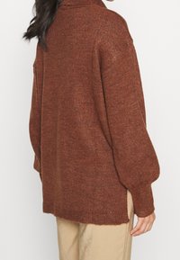 Brązowy sweter wykonany na drutach z wysokim kołnierzem, długimi rękawami i lekko oversize'owym krojem. Charakteryzuje się teksturowanym wykończeniem i bocznymi rozcięciami.