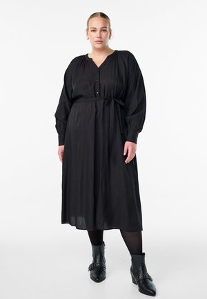 Sort langærmet kjole med knaplukning foran, bælte i taljen og plisseret tekstur. Sammen med ankelstøvler med dekorativt metal.