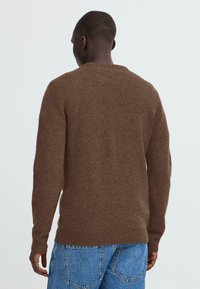 Brauner Strickpullover mit ribbeligem Rundhalsausschnitt und langen Ärmeln, der eine weiche Textur und einen dezenten Glanz aufweist, kombiniert mit blauen Jeans.
