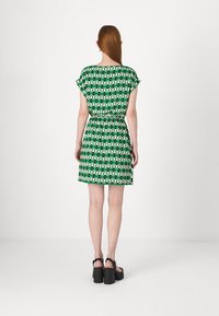 Short green dress with a geometric black and white pattern, short sleeves, elastic waist, and a flared skirt. Black chunky heeled sandals.