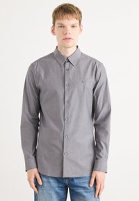 Camisa de manga larga a rayas grises con cuello abotonado, que presenta finas rayas verticales y un pequeño logo en el pecho.
