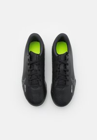 Un par de botas de fútbol Nike Mercurial negras con cordones y plantillas de neón verde, vistas desde arriba sobre un fondo blanco.