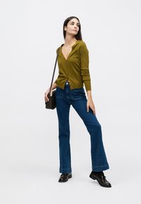 Cardigan boutonné vert olive associé à un jean en denim foncé taille haute évasé. Chaussures noires et petit sac bandoulière marron.